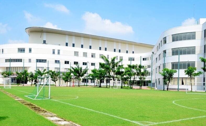 잔디 축구장과 골대 너머로 보이는 흰색 곡선형 교사와 그 앞의 나무들