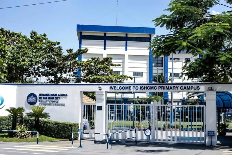 ISHCMC 초등 캠퍼스 정문 — 학교 이름이 적힌 흰 담장과 그 뒤의 흰색 · 파란색 건물