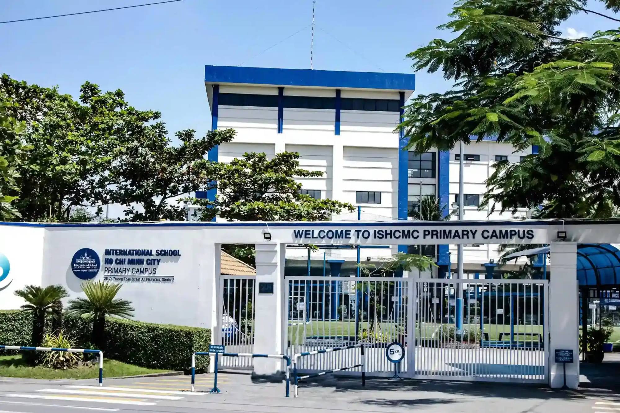 ISHCMC 초등 캠퍼스 정문 — 학교 이름이 적힌 흰 담장과 그 뒤의 흰색 · 파란색 건물